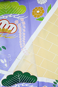 黄色いレンガ、白い斜めの線、緑の葉、紫色の装飾部分からなるカラフルな模様の布のアップ。.