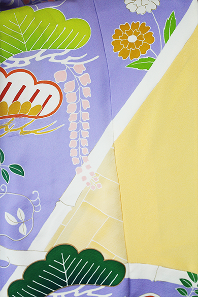 緑と黄色の植物、白い幾何学的な線、オレンジと白の花、淡い紫色を背景にしたカラフルな模様の布地のアップ。.