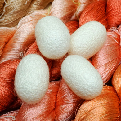 オレンジと桃色の絹糸の上に、4つの白い蚕の繭が美しく束ねられている。お手入れはシルクの繊細な風合いを保つために重要で、コレクターや愛好家にとって役立つ豆知識です。.